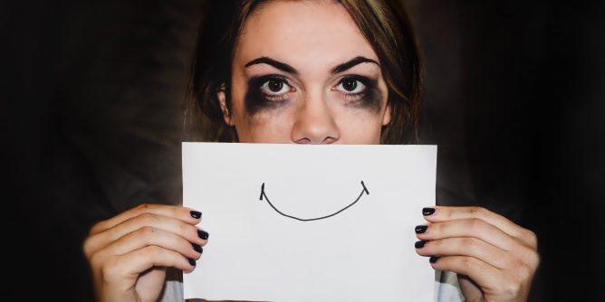 Depressed girl holding up sign of fake smiley face